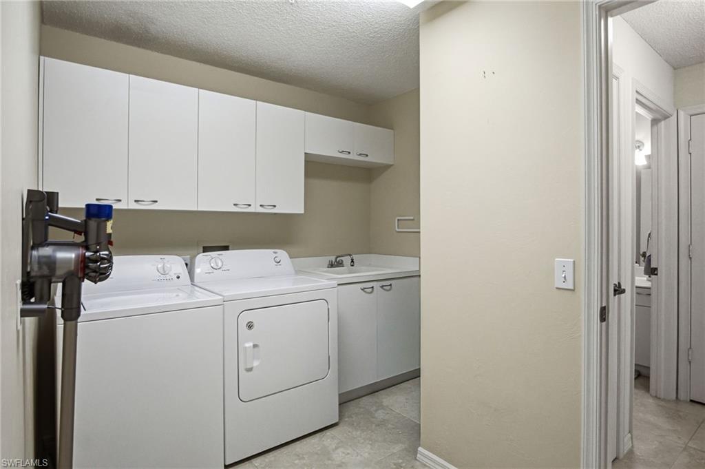 Dedicated laundry room featuring side-by-side white appliances, ample cabinetry with overhead storage, stainless steel sink with faucet, concrete flooring, and direct access to additional living spaces
