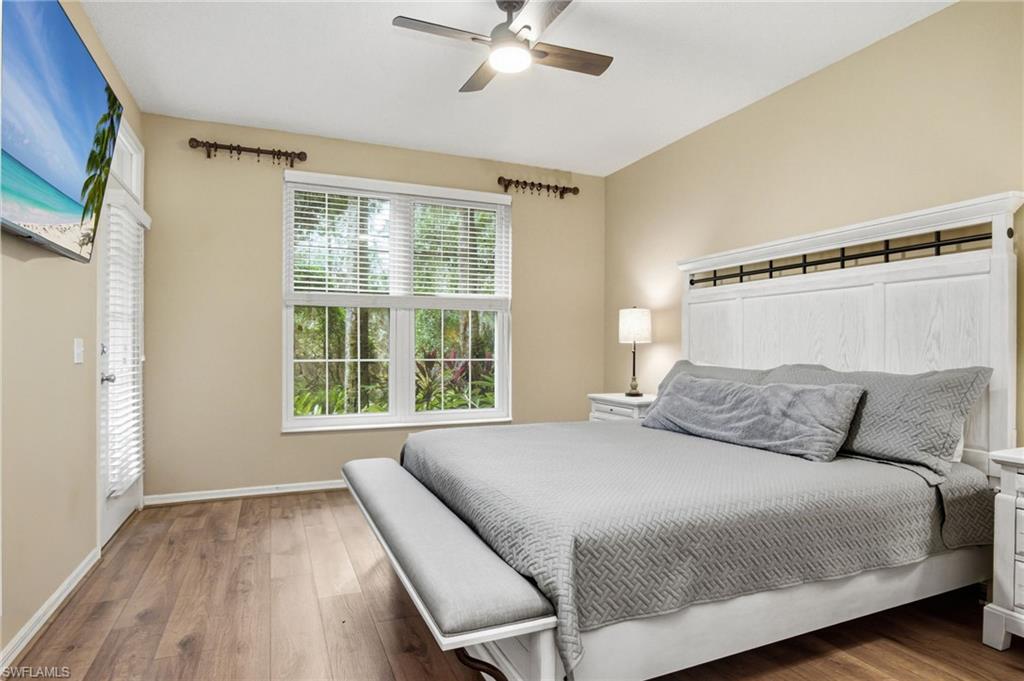Vaulted ceiling room featuring wood-finish flooring, a ceiling fan with integrated lighting, a multi-pane window with blinds, and an exterior door with louvered glass