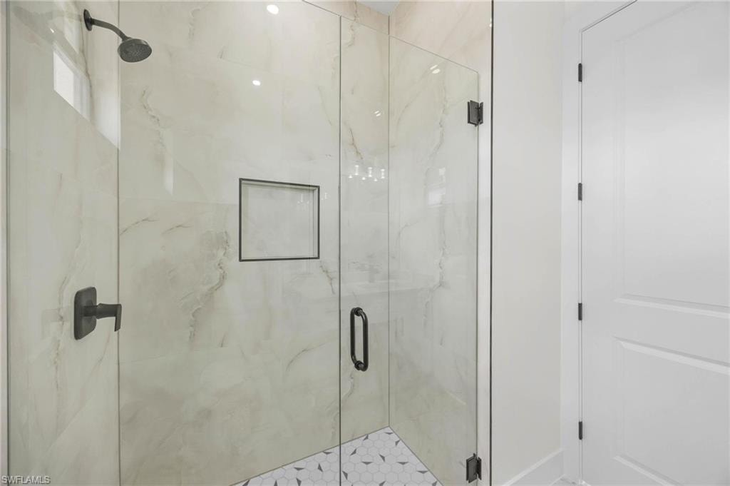 Glass-enclosed shower featuring large format tile walls, a built-in niche, and a hexagonal mosaic tile floor