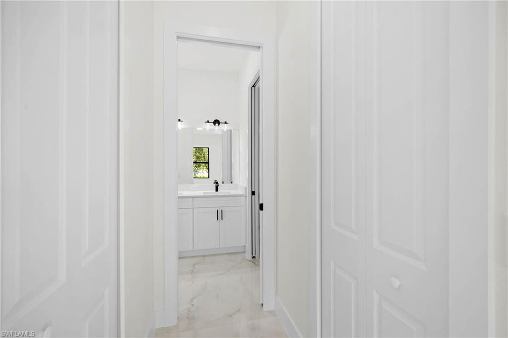 Hallway with white bi-fold doors, leading to a bathroom featuring a white vanity with double sinks, a window with exterior views, and a large mirror with a three-bulb light fixture