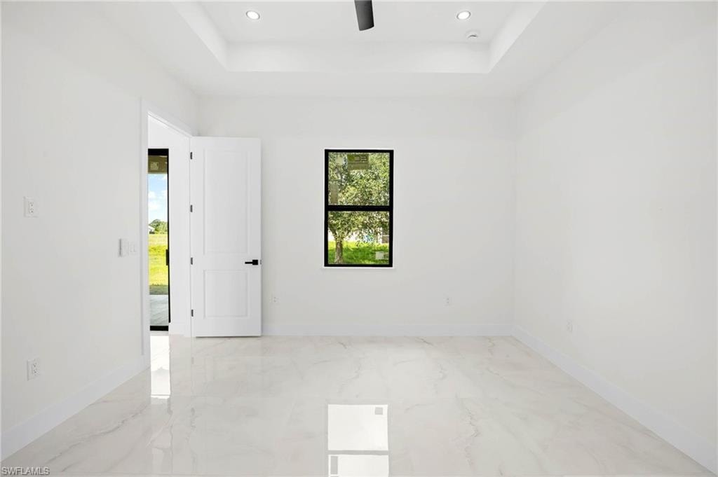 Bright interior room featuring white walls, large format tile flooring, and a tray ceiling with recessed lighting
