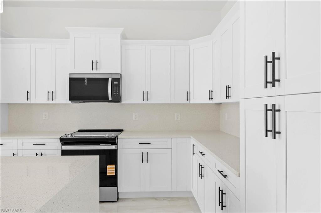 Modern kitchen featuring white shaker cabinetry, stainless steel appliances, light-toned countertops, and a full-height backsplash