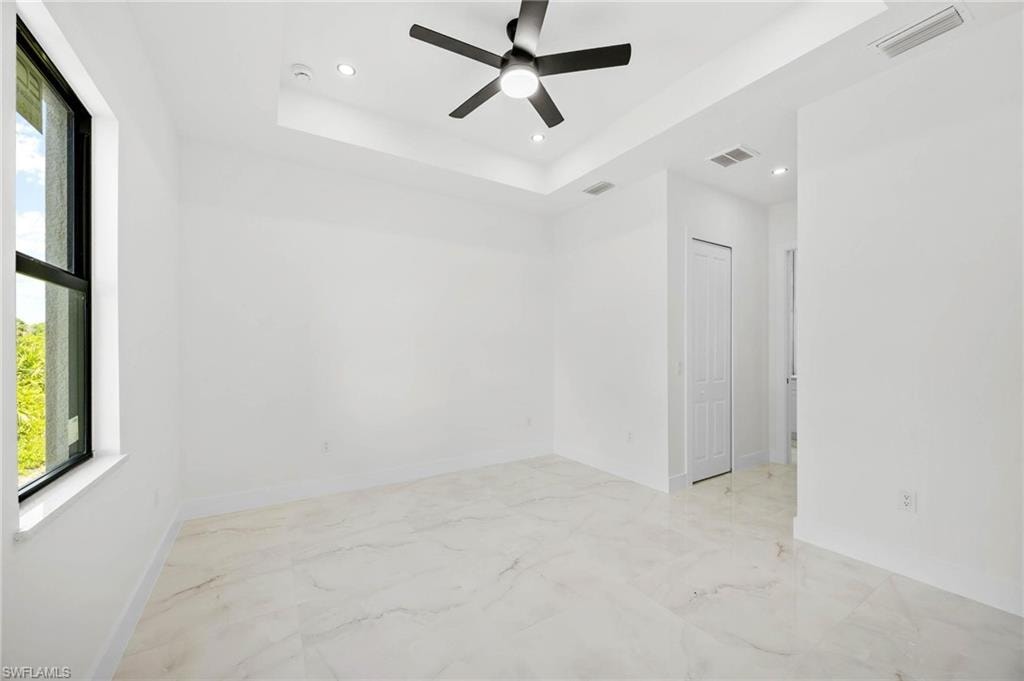 Spacious interior room featuring a large window, tray ceiling with recessed lighting, ceiling fan, and large format tile flooring