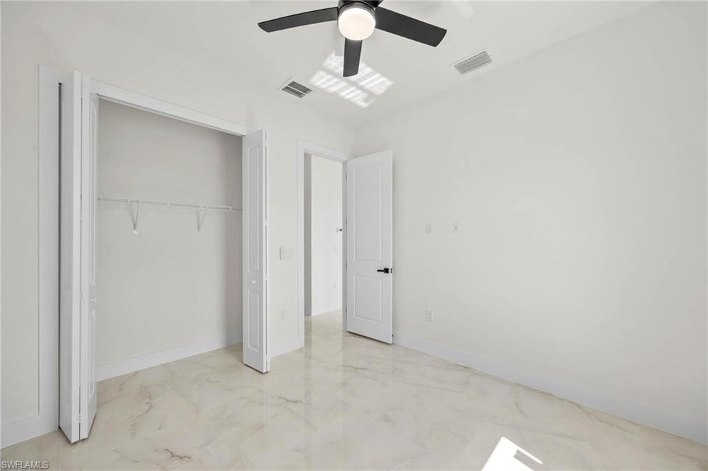 Room featuring polished marble-look flooring, a ceiling fan with integrated lighting, and a bi-fold closet with built-in shelving