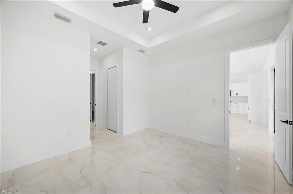Spacious interior featuring large format tile flooring, a tray ceiling with recessed lighting, and a black ceiling fan