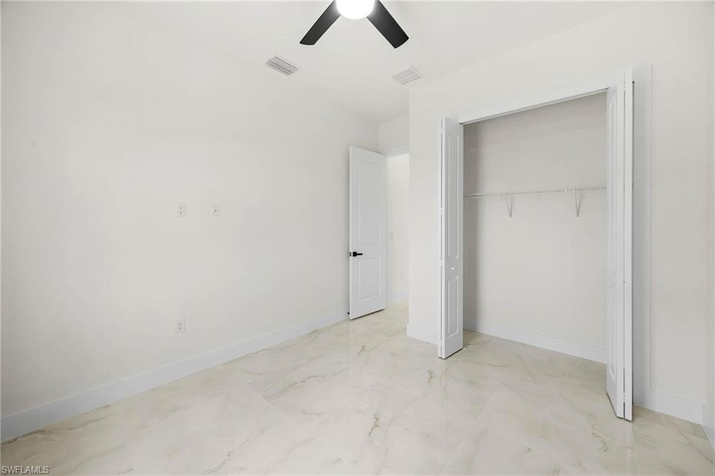 Room featuring light-toned large format tile flooring, white walls, and a ceiling fan with black blades
