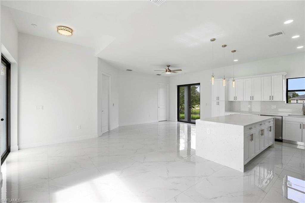 Open-concept living space featuring sleek white tile flooring, a contemporary kitchen island with a light-toned countertop, white cabinetry, and stainless steel appliances