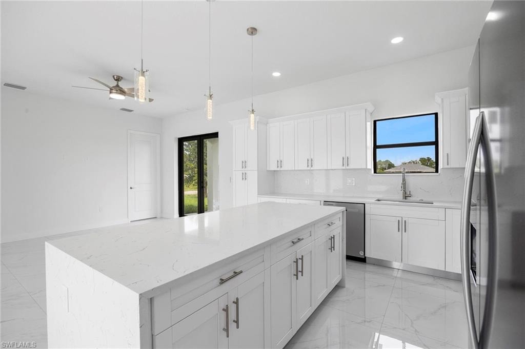 Expansive kitchen island with a light-toned countertop, complemented by white cabinetry, stainless steel appliances, and large format tile flooring