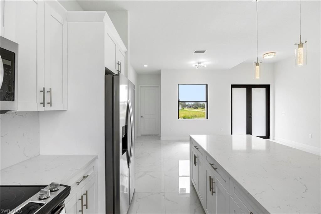 Modern kitchen and living area featuring a large center island with a light-toned countertop, white cabinetry with contemporary hardware, stainless steel appliances, and white tile flooring