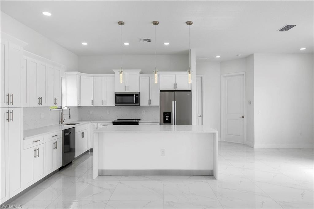 Modern kitchen featuring white shaker cabinetry, stainless steel appliances, a center island, recessed lighting, and large format tile flooring