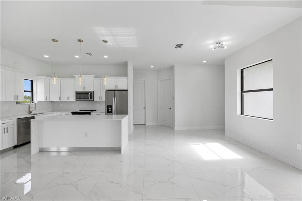 Spacious kitchen and living area featuring a large center island, white cabinetry, stainless steel appliances, and large format tile flooring