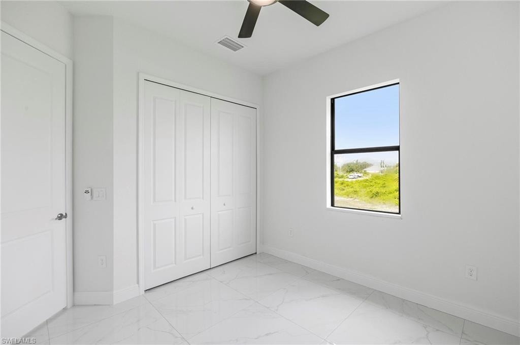 Bright room featuring a square window, white bi-fold closet doors, a ceiling fan, and large format tile flooring