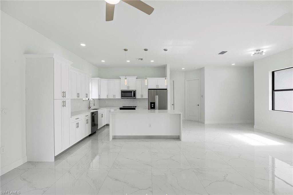 Open-concept kitchen featuring white shaker cabinetry, stainless steel appliances, a central island, recessed lighting, and large format marble-look tile flooring