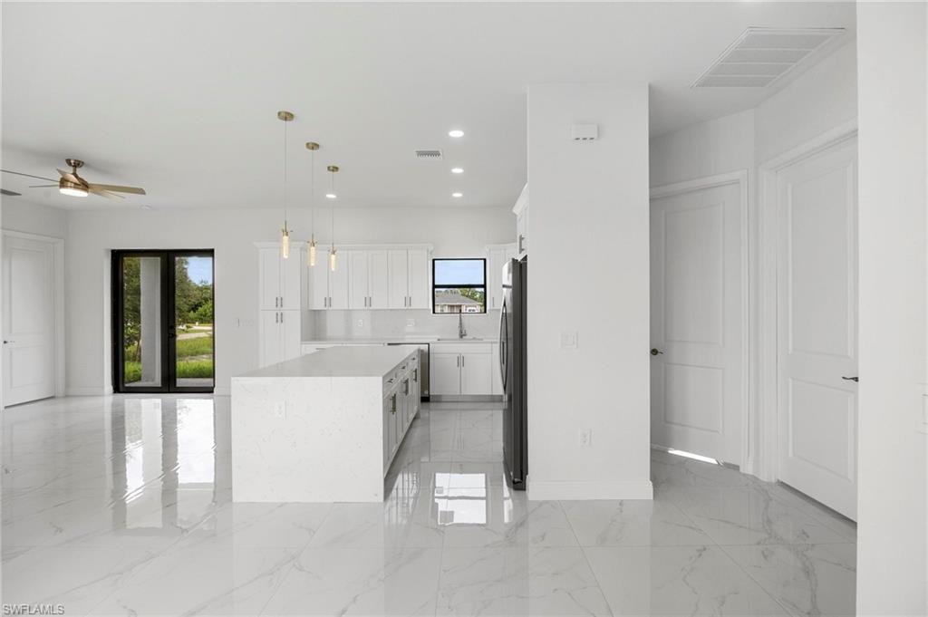 Open-concept living area featuring a kitchen island with a waterfall countertop, white flat-panel cabinetry, and stainless steel appliances