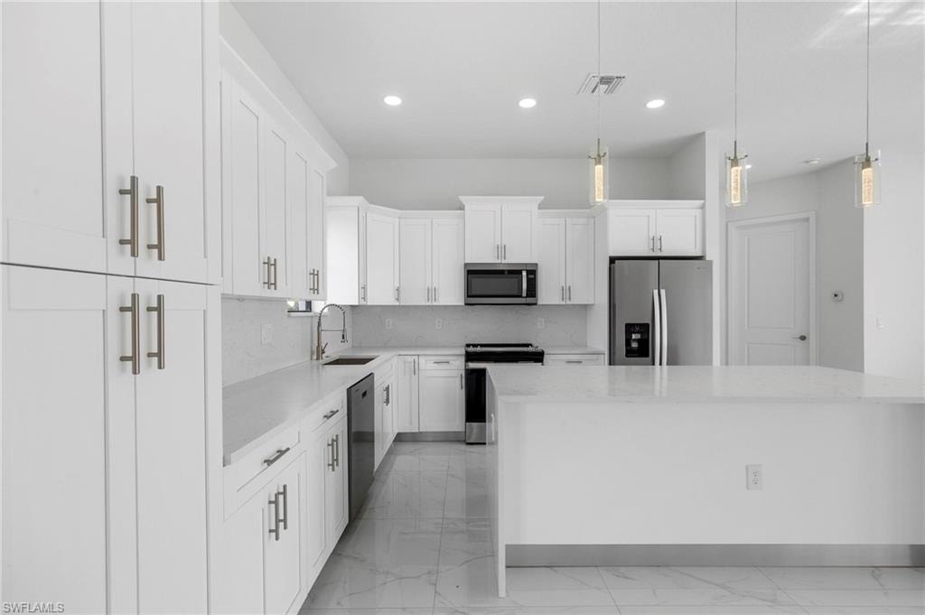 Modern kitchen featuring white shaker cabinetry, stainless steel appliances, a center island with countertop seating, recessed lighting, and pendant fixtures