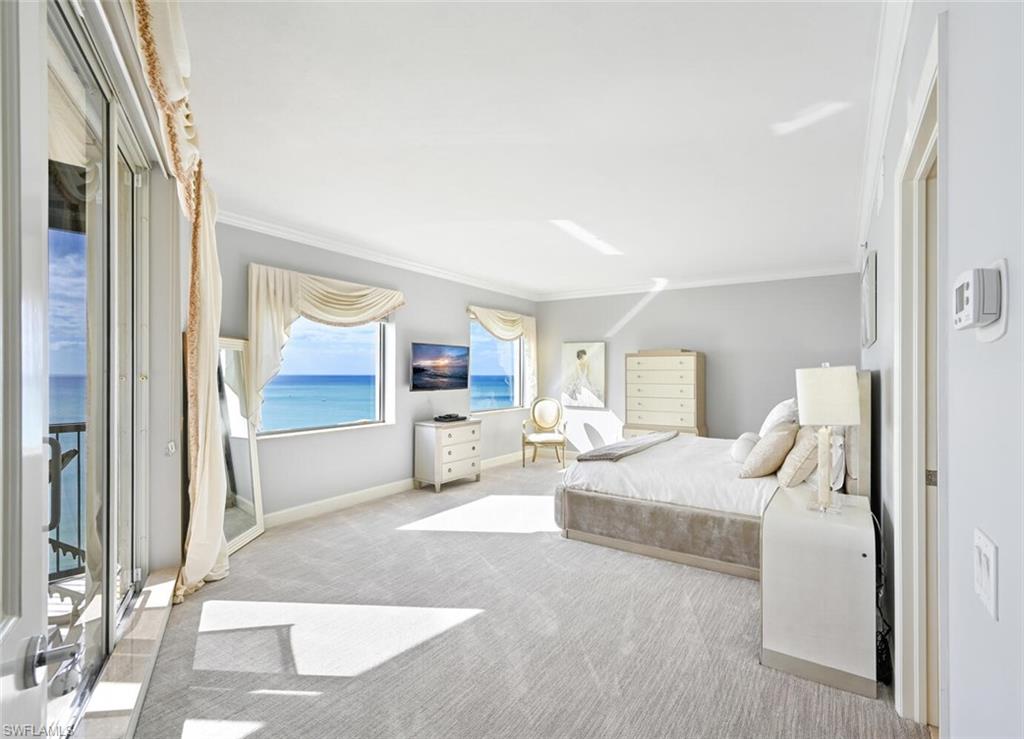 Oceanfront bedroom featuring direct balcony access, expansive windows with water scenery, crown molding, and light-toned wall finishes