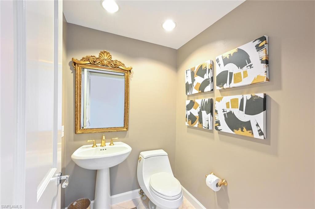 Pedestal sink with brass-finish faucet, framed mirror, and recessed lighting