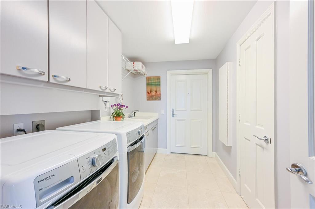 Laundry room featuring extensive white cabinetry, a built-in utility sink, and light-toned tile flooring