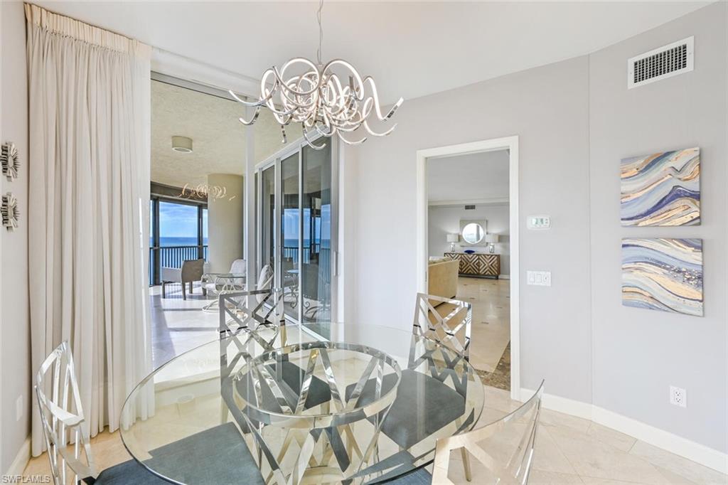 Open dining area featuring a modern chandelier, light-toned wall paint, and a glass-top dining table with metallic chairs