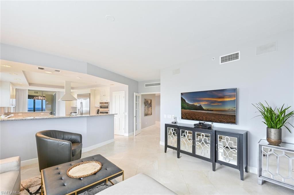 Open-concept living space featuring light-toned tile flooring, recessed lighting, and a kitchen pass-through with a breakfast bar