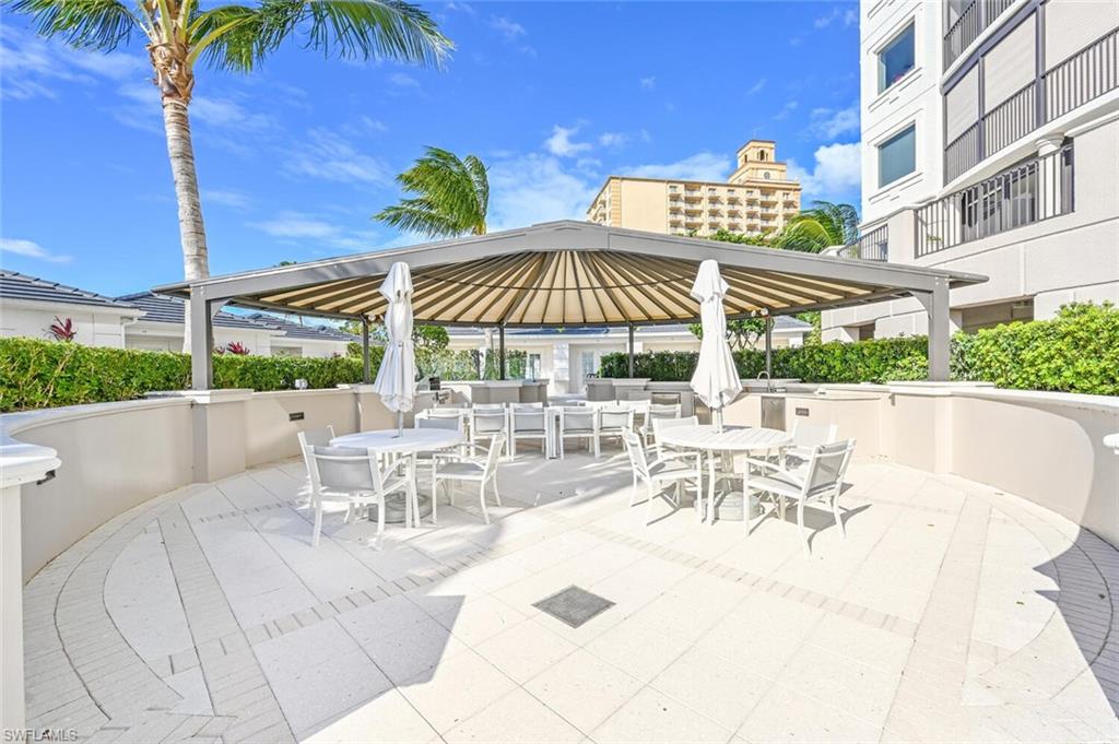 Outdoor patio area featuring a large pergola, white paver flooring, built-in outdoor cooking station, and mature landscaping