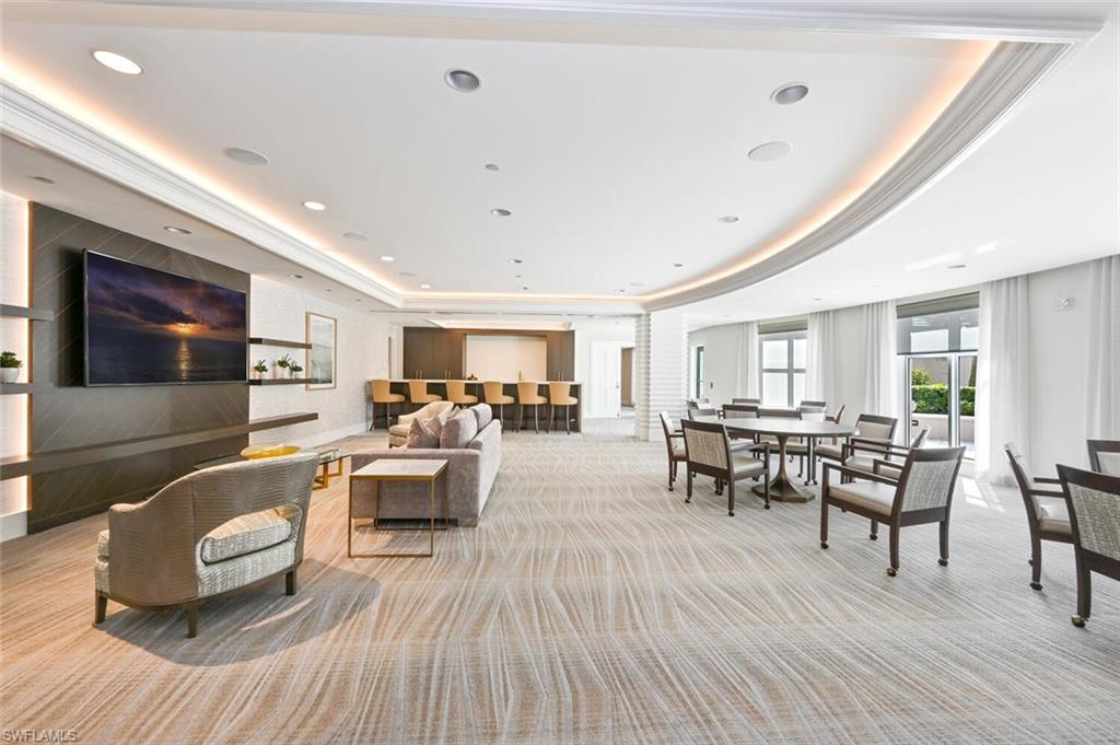 Spacious common area featuring textured carpeting, recessed lighting, a built-in media wall with shelving, a bar area with counter seating, and multiple seating arrangements