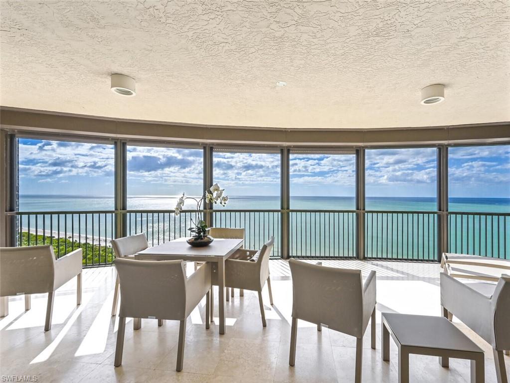 Expansive balcony featuring floor-to-ceiling windows, panoramic ocean scenery, light-toned flooring, and contemporary overhead lighting fixtures