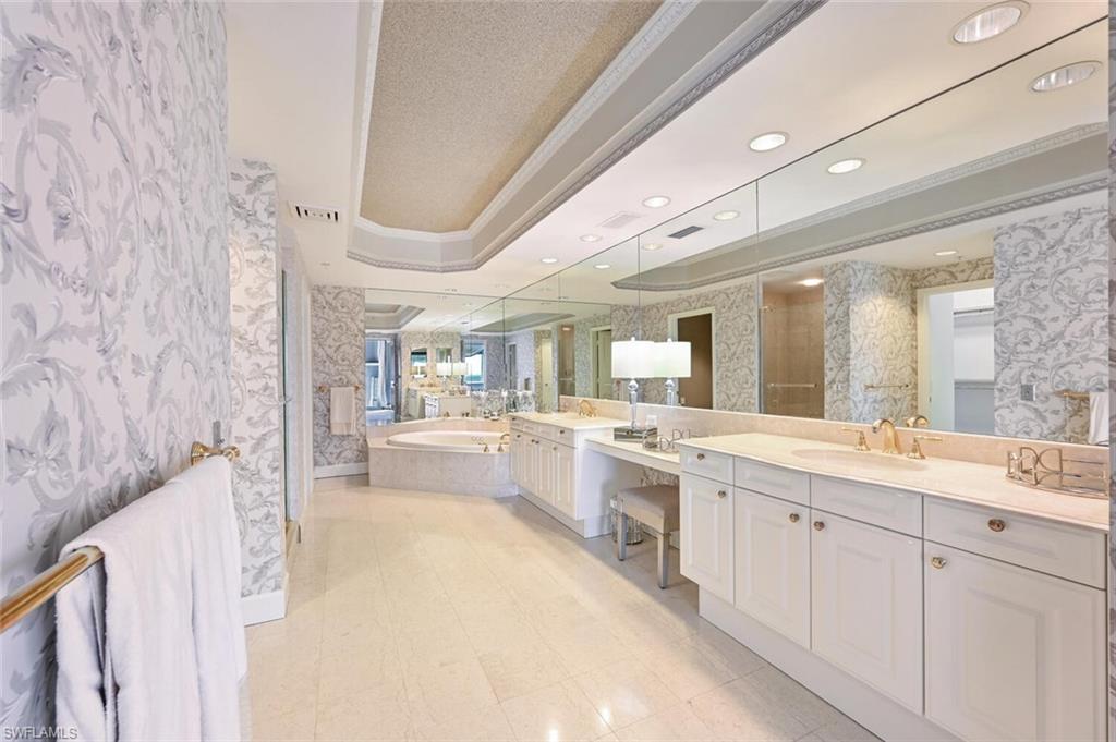 Spacious bathroom featuring dual vanities with integrated sinks, a built-in makeup area, a jetted soaking tub, and extensive mirror coverage