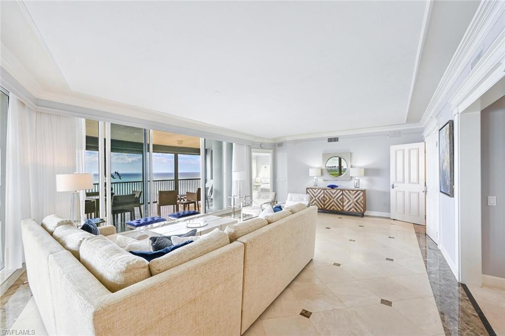 Spacious living area featuring large format tile flooring, crown molding, and expansive sliding glass doors opening to a balcony with water scenery