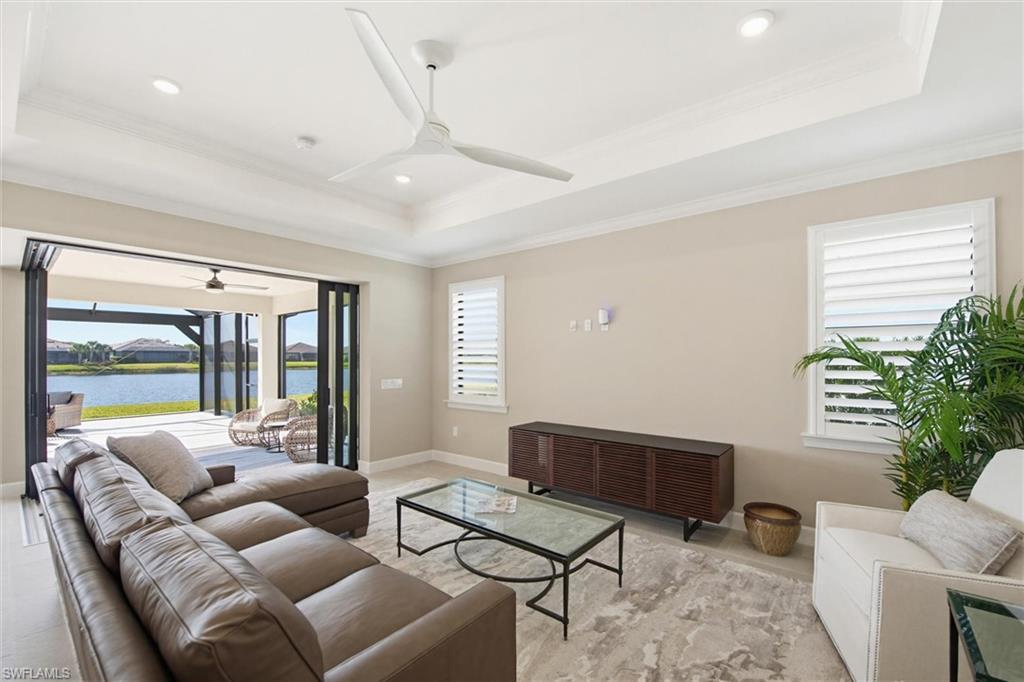 Living room featuring a tray ceiling, ceiling fan, ornamental molding, healthy amount of natural light, and a water view