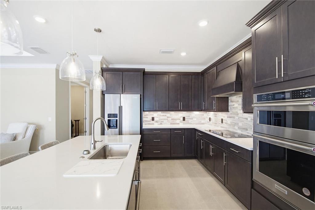 Kitchen with stainless steel appliances, crown molding, hanging light fixtures, dark wood finish cabinetry, and tasteful backsplash