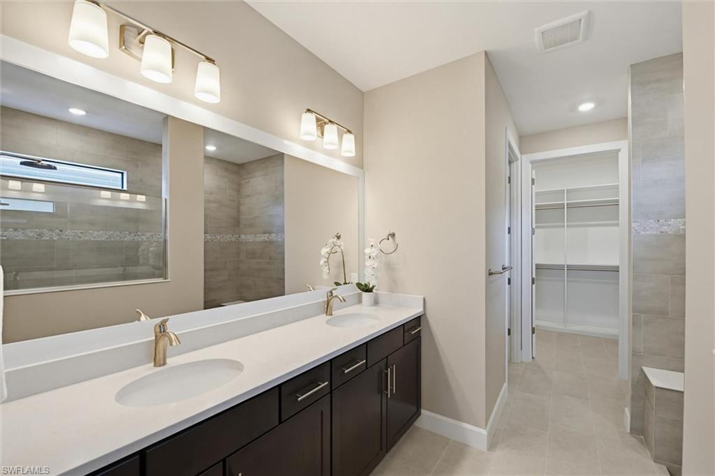 Full bathroom featuring a spacious closet, double vanity, walk in shower, recessed lighting, and light tile patterned floors