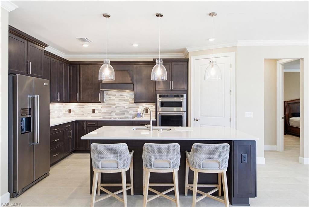 Kitchen with stainless steel appliances, dark wood finish cabinetry, a breakfast bar, ornamental molding, and light stone countertops