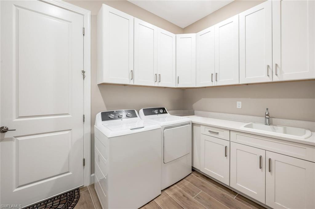 Laundry area featuring white shaker-style cabinetry, a built-in sink with a chrome faucet, light-toned countertops, and wood-finish tile flooring