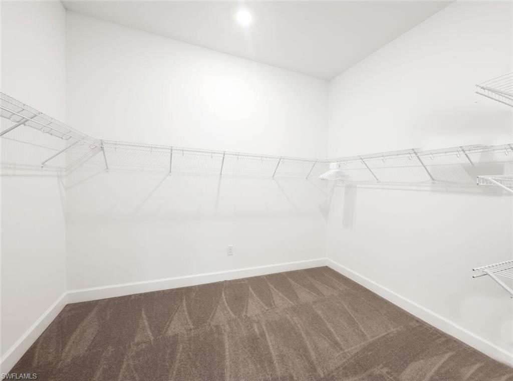 Spacious walk-in closet featuring white wire shelving, bright white walls, recessed ceiling lighting, and soft grey carpeting