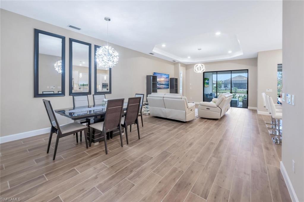 Open-concept interior featuring wood-finish flooring, a tray ceiling with recessed lighting, and a modern dining area with a statement chandelier