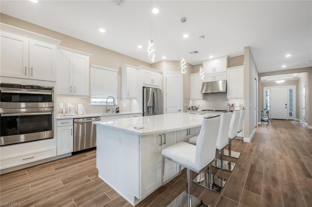 Modern kitchen featuring white shaker cabinetry, stainless steel appliances, a center island with countertop seating, recessed lighting, and wood-finish flooring