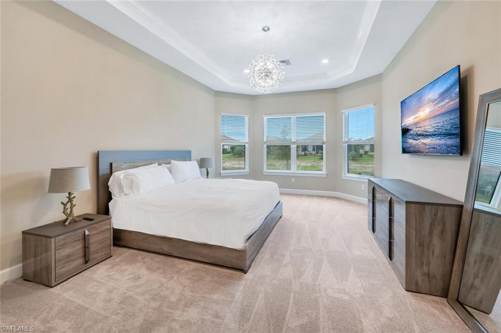 Spacious room featuring neutral carpeting, a tray ceiling with crown molding, and a contemporary chandelier
