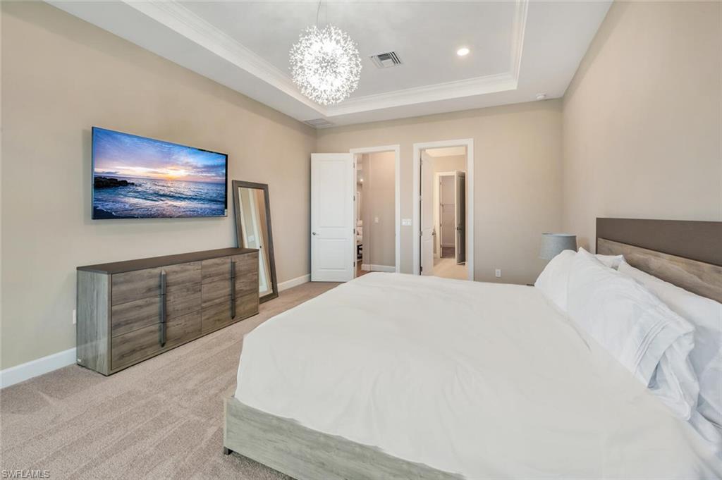 Spacious bedroom featuring neutral wall tones, tray ceiling with recessed lighting, and a modern chandelier