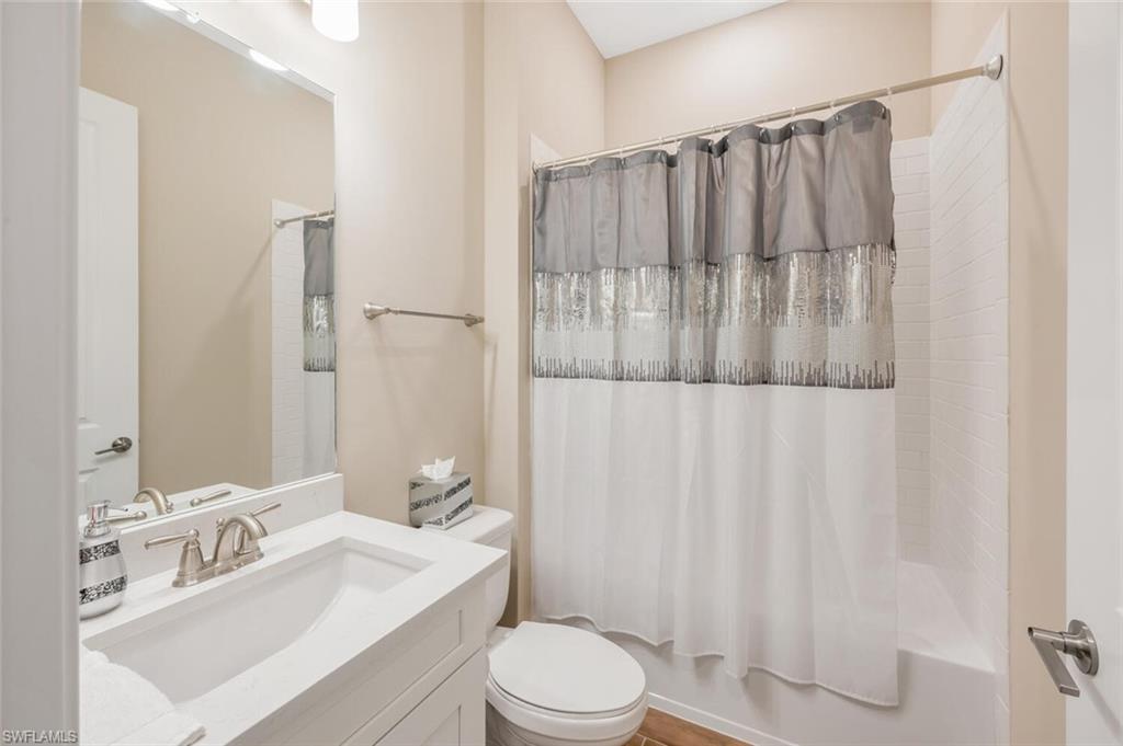 Bathroom featuring a white vanity with an integrated sink, brushed nickel faucet, large wall mirror, and a shower-over-tub with white subway tile surround