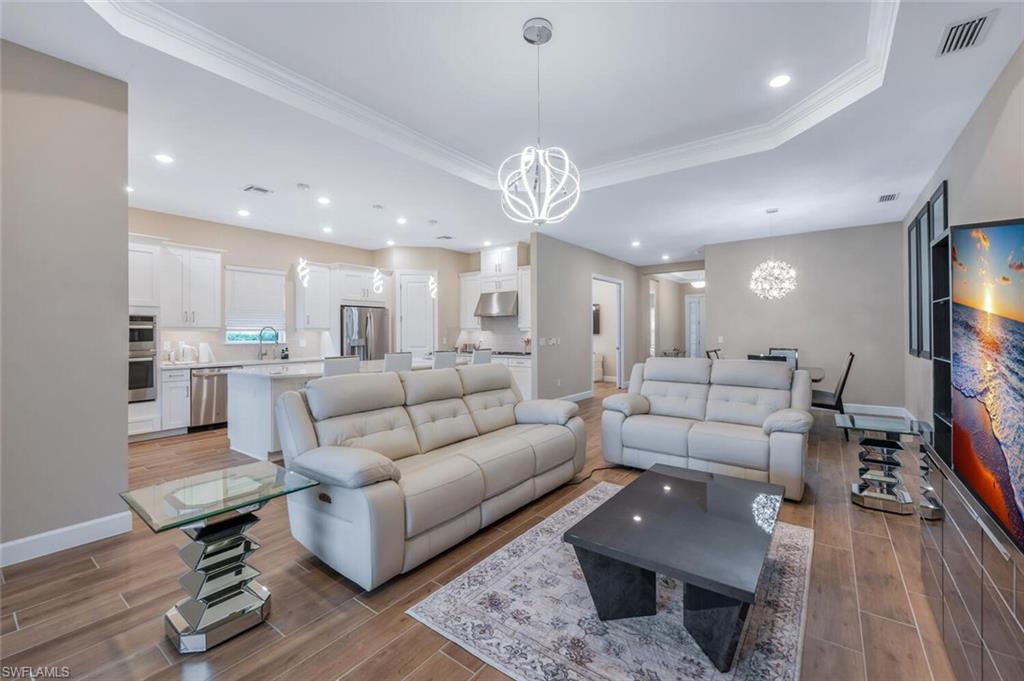 Open-concept living space featuring wood-finish tile flooring, recessed lighting, crown molding, and a contemporary chandelier