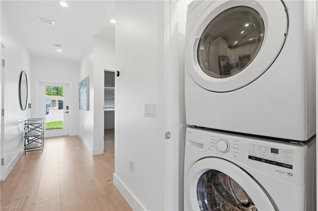 Stackable washer and dryer unit with a light wood-finish flooring hallway