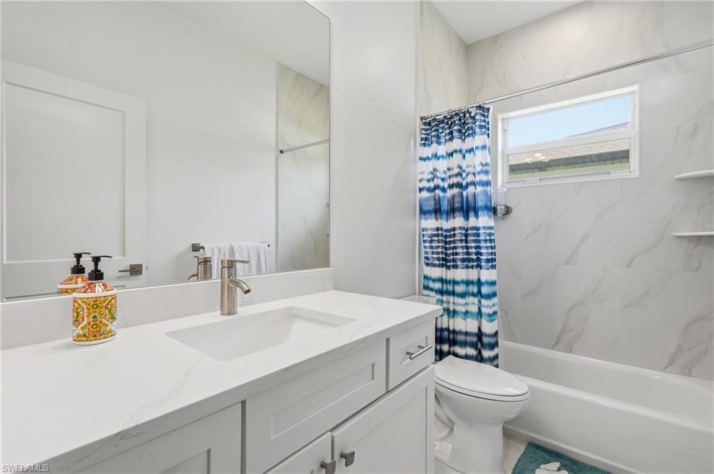 Bathroom featuring a white vanity with an integrated sink, brushed nickel faucet, large wall mirror, and a full bathtub with white tiled surround