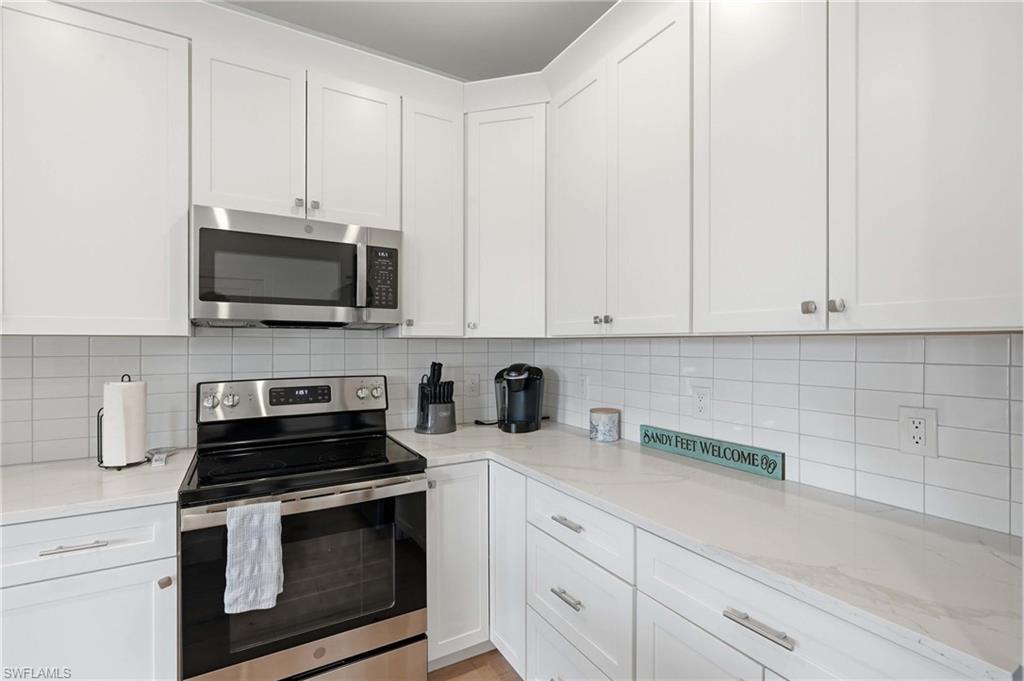 White cabinetry with stainless steel appliances, light-toned countertops, and a white subway tile backsplash