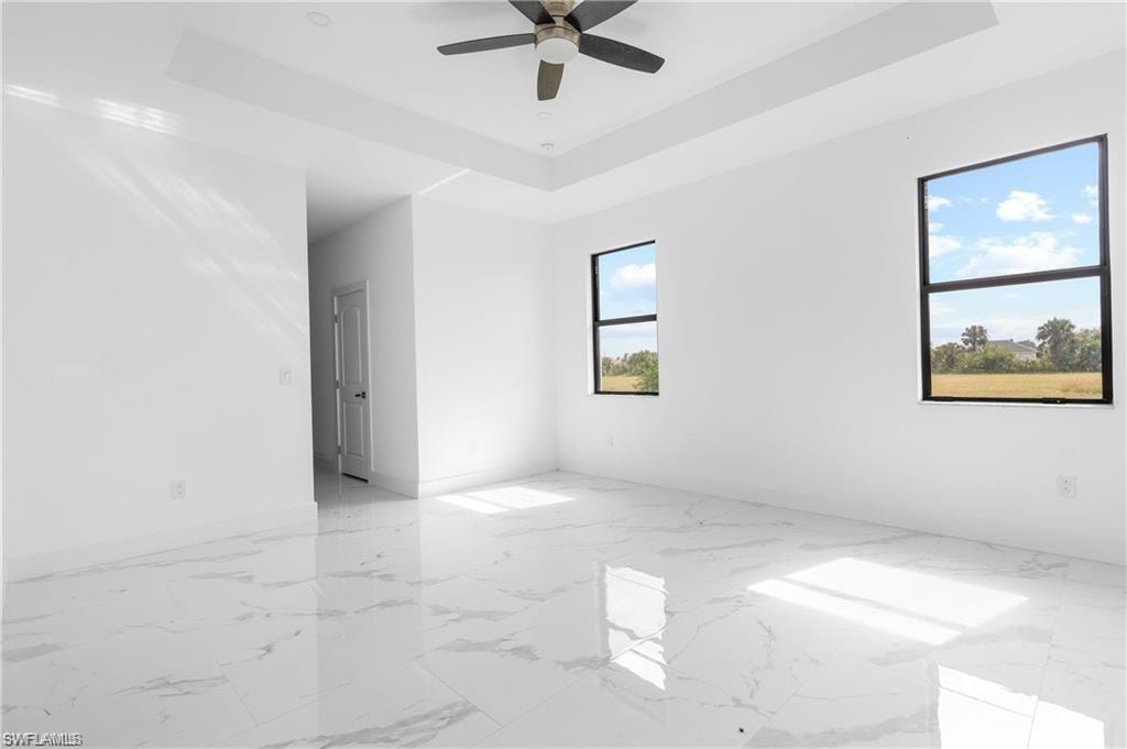 Expansive room featuring white walls, large format tile flooring, a tray ceiling, and a ceiling fan