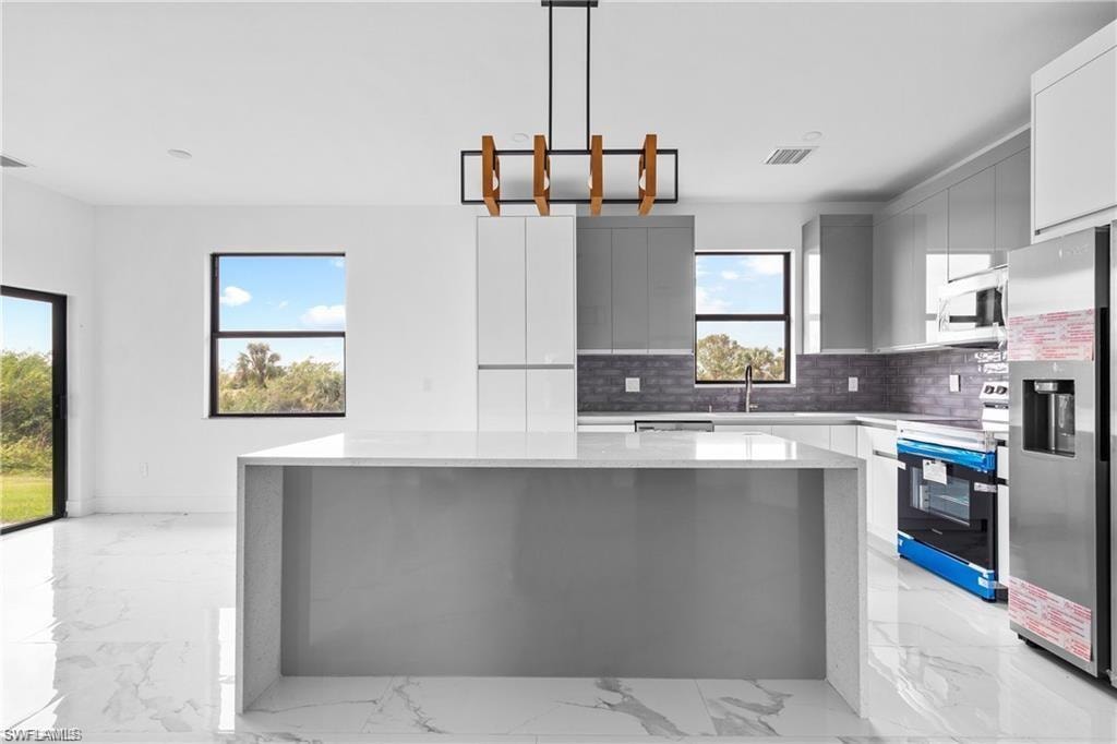 Modern kitchen featuring a waterfall island with a light-toned countertop, white and gray cabinetry, and a dark tile backsplash