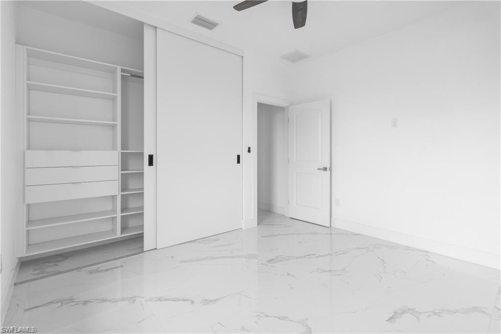 Room featuring large format tile flooring, white walls, a built-in closet with sliding doors, and a ceiling fan