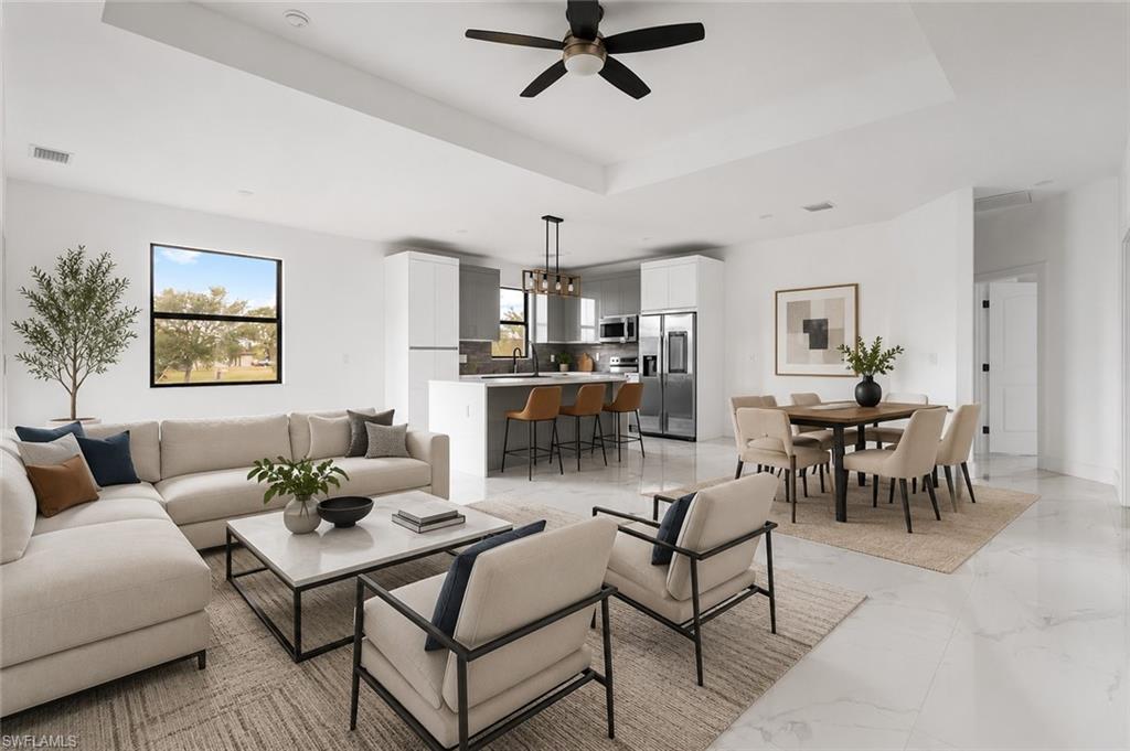 Spacious living area featuring large format tile flooring, a tray ceiling with a ceiling fan, a kitchen island with seating, and a dining area