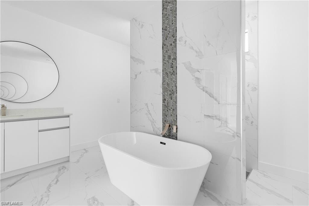 Freestanding soaking tub set against a marble-finish accent wall with a vertical mosaic tile inlay