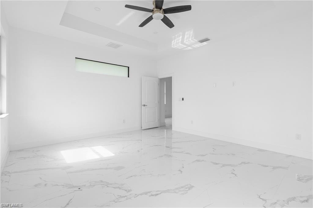 Spacious interior room featuring large format tile flooring, a tray ceiling, and a ceiling fan
